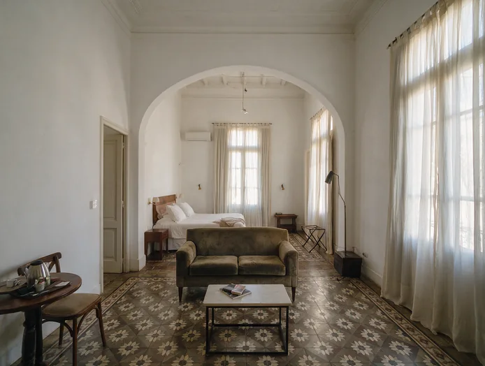 Suite con living de pana y el dormitorio detrás del arco